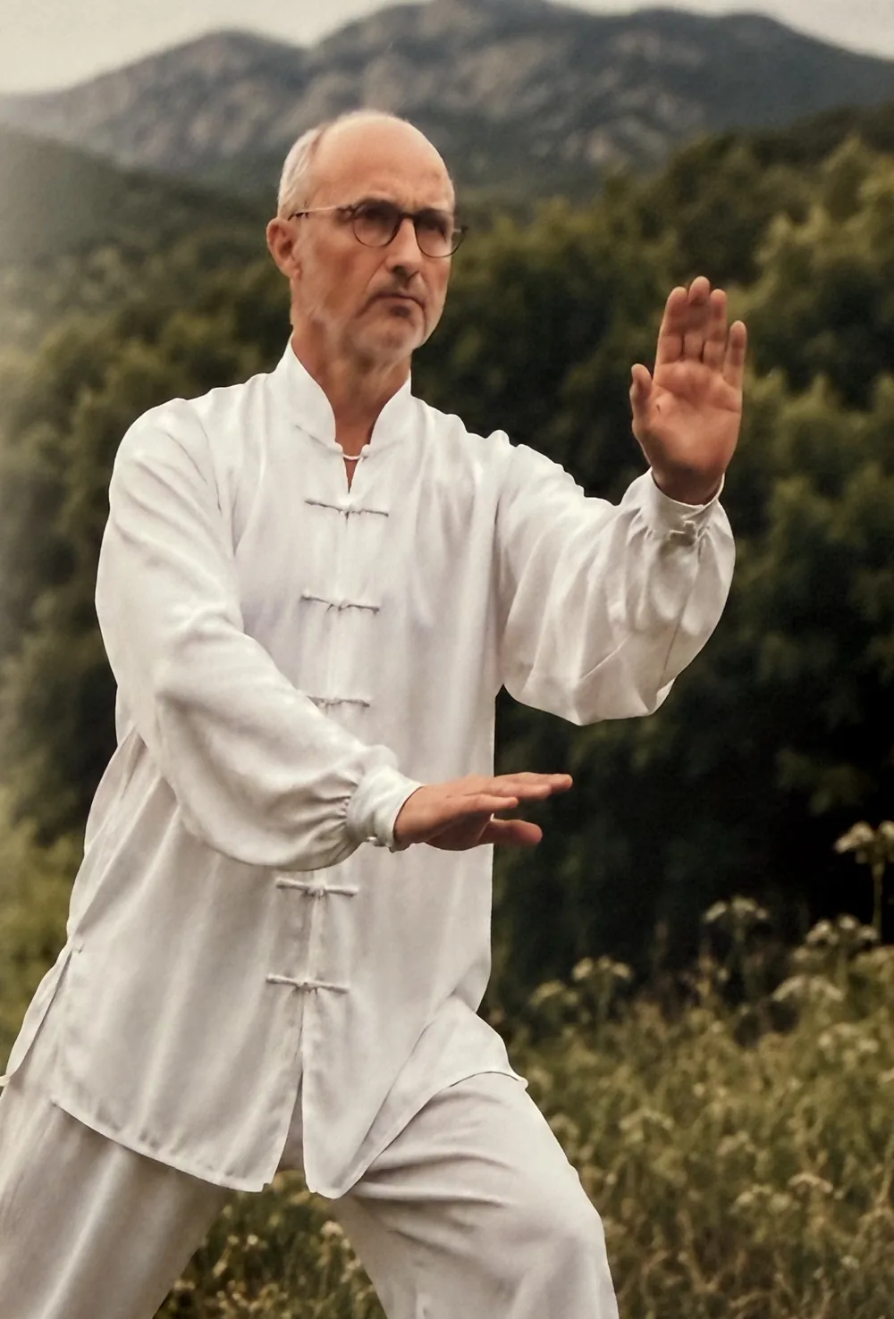 Jean-Fabien Darotte en tenue blanche, en posture de Tai Chi Chuan en extérieur face aux collines